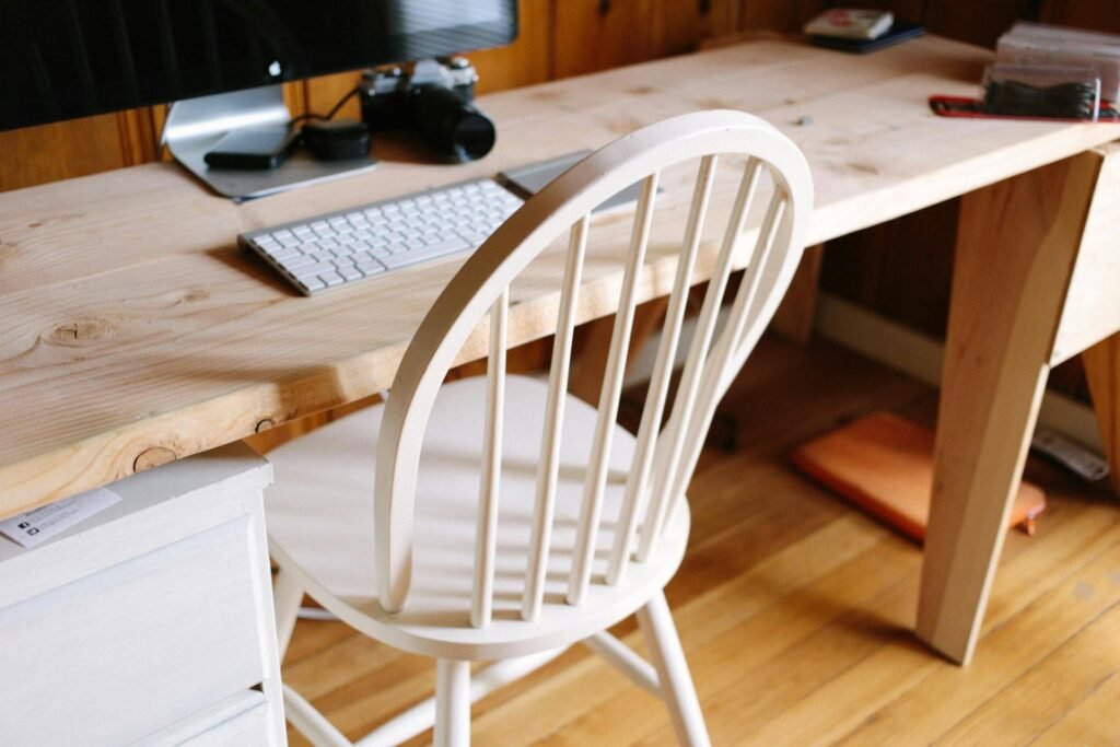A minimalist home office setup with a wooden desk, chair, keyboard, and camera.